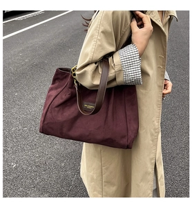 Close-up of a burgundy tote bag featuring leather straps and a golden brand logo plate