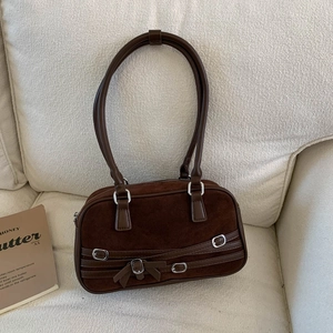 Detailed view of brown suede bowling bag with silver buckles on a cozy sofa