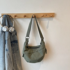 Detail view of dark green canvas crescent bag with adjustable strap on a wooden hook