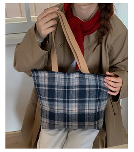 Classic large plaid tote bag in blue and grey with wide tan straps styled on a trench coat