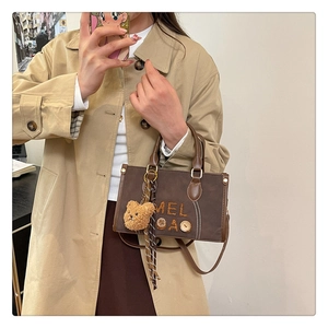 Détail d'un sac bandoulière en daim marron avec boutons vintage et pendentif ours