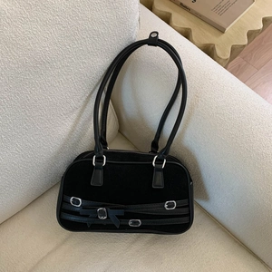 Detail of black bowling bag with decorative straps and bow on a beige sofa background