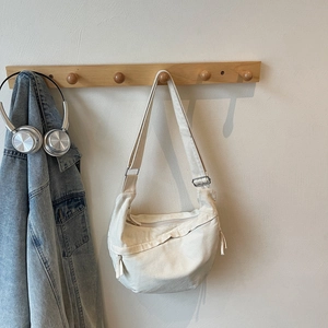 Detail of minimalist cream canvas crossbody bag hanging on hook with adjustable strap