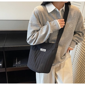 Detail of black quilted crossbody bag with white LOVE patch and thick shoulder strap