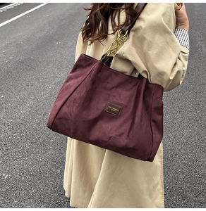 Close-up of burgundy tote bag with chain strap and branding on beige trench coat