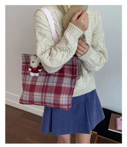 Detail of red and blue plaid tote bag featuring a cute white teddy bear plush charm