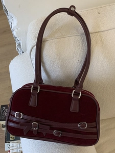 Minimalist burgundy suede bowling shoulder bag with cross-straps and bow detail on a sofa