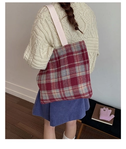 Detail of red plaid wool tote bag with pink strap worn by model in cozy autumn setting