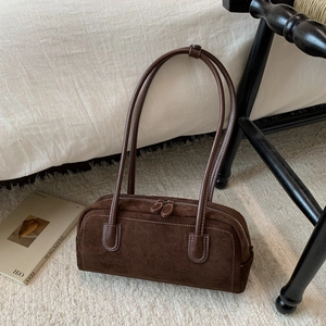 Detailed close-up of dark brown suede cylinder bag with white stitching on white rug