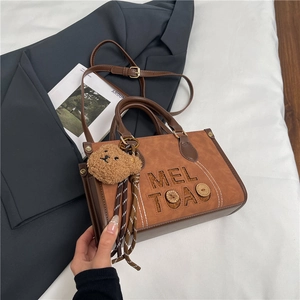 Détail d'un sac à main marron rétro avec gravure MEL TOAO et pendentif ours en peluche