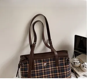 Close-up of plaid tote bag featuring a teddy bear embroidery and brown leather handles