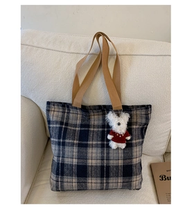 Close-up of woven plaid tote bag with khaki straps and a cute plush bear charm