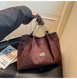 Detail of burgundy suede tote bag with elegant gold chain strap and gathered pleat texture