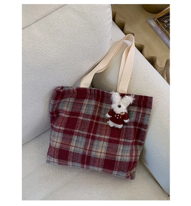 Detail of red and grey woven plaid tote bag with cute plush pendant on a soft sofa