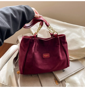 Detail of burgundy suede tote bag featuring premium gold chain handles and logo plaque