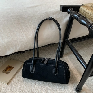 Detailed view of black suede baguette bag with contrast stitching on soft carpet