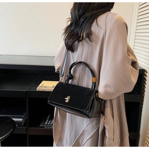 Detail shot of a minimalist black handbag featuring a gold buckle and suede texture mix