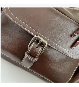 Detailed macro view of silver metal buckle with white stitching on brown leather bag