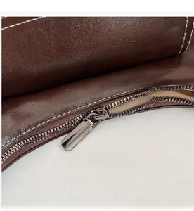 Macro detail of high-quality smooth metal zipper and white stitching on brown leather bag