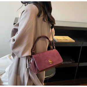 Detail of burgundy textured leather handbag featuring a vintage gold twist lock closure