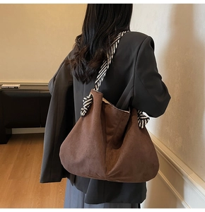Detail view of large brown suede tote bag with striped woven strap and side knot details