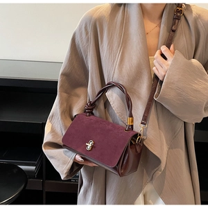 Detail of burgundy faux suede and leather handbag with golden twist lock and knot handle