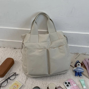 Detail of light beige multi-pocket nylon tote bag with drawstring sides on a white rug
