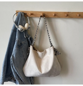 Detail of white suede tote bag with striped woven shoulder strap hanging on a wooden hook