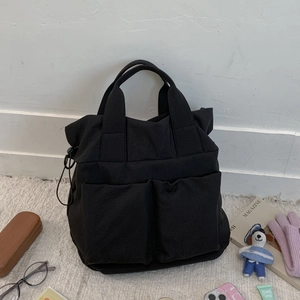 Detail of black canvas tote bag showing large front pockets and drawstring toggle side