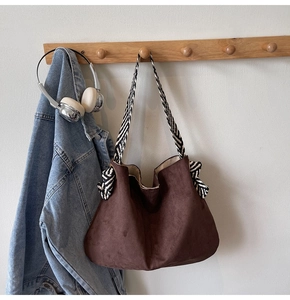Close-up of brown suede hobo bag with a black and white striped woven wide shoulder strap