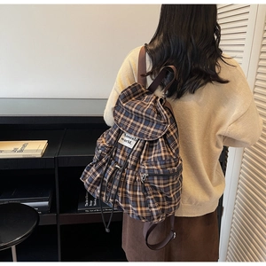 Detail showing vintage plaid backpack texture with flap drawstring and woven logo label