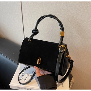Detail of black leather square bag with suede flap, gold hardware and knot handle detail