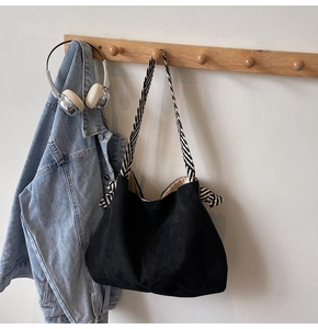 Detail of black suede tote bag featuring a stylish black and white striped woven strap