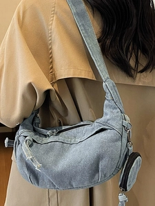 Grand sac demi-lune en jean bleu avec porte-monnaie porté par un mannequin en trench