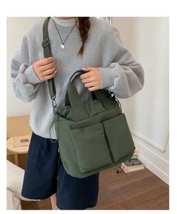 Detail of dark green nylon tote with large front pockets and adjustable strap shown on model