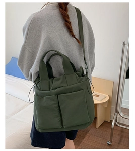 Detail of dark green nylon tote bag with dual front pockets and adjustable strap