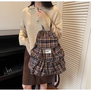 Detail view of a vintage plaid backpack showing side zipper pockets and woven straps