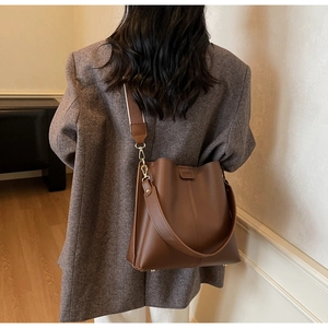Détail d'un sac seau en cuir marron foncé avec large bandoulière tissée sur un modèle