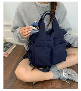 Deep blue nylon multi-pocket tote bag with a cute plush charm worn in a lifestyle setting