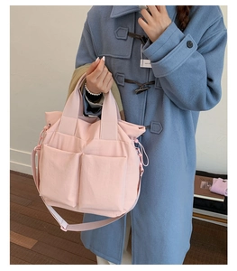 Close-up of pink multi-pocket nylon crossbody bag with side drawstring and woven strap