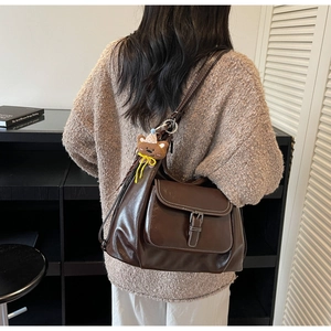 Close-up of a retro dark brown leather tote bag with a decorative cute bear pendant