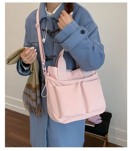 Detail of a large pink crossbody bag with front pockets and adjustable shoulder strap