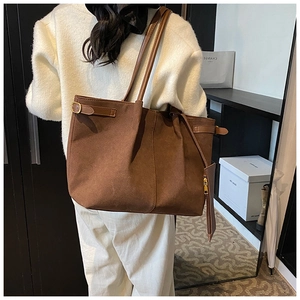 Detail of a brown suede tote bag featuring a side metal buckle and matching small pouch