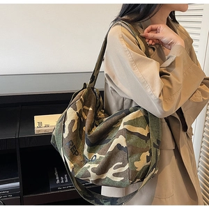 Détail du sac cabas en toile camouflage porté par un mannequin dans un décor moderne