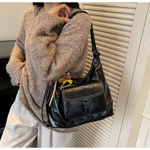 Close-up of black leather tote bag with white contrast stitching and bear keychain
