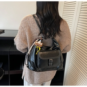 Detail of black faux leather backpack with white stitching and cute bear charm pendant