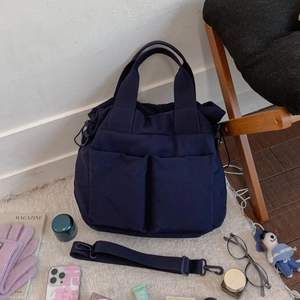 Detail of navy nylon tote bag with front pockets and adjustable strap in lifestyle setting