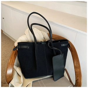 Detail view of black suede tote bag with side buckles and matching mini pouch on a chair