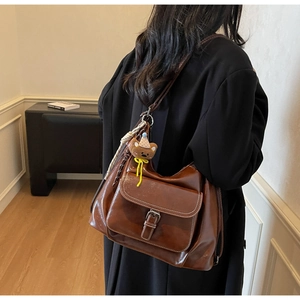 Brown leather shoulder bag featuring white contrast stitching and a cute bear charm pendant