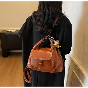 Detail of vintage brown leather backpack featuring a front pocket and cute bear charm